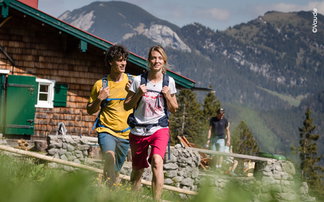 Wanderer in T-Shirts und kurzen Hosen vor einer Hütte in den Bergen.