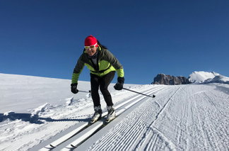 Mann mit Langlaufskiern fährt auf Loipe bergab