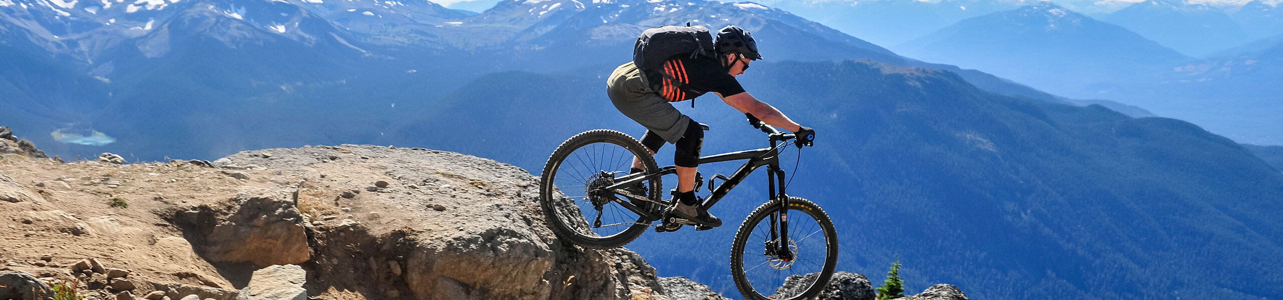 Einzelner Mountainbiker vor Bergkulisse fährt Downhill