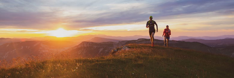 two trail runners running across a meadow in the sunset