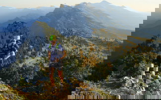 Trailrunner läuft über Berggrad bergauf mit Bergen im Hintergrund