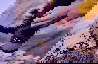 Schuh von Salewa, Mensch bindet Schuhband auf Fels, Fokus auf grau orangem Schuh